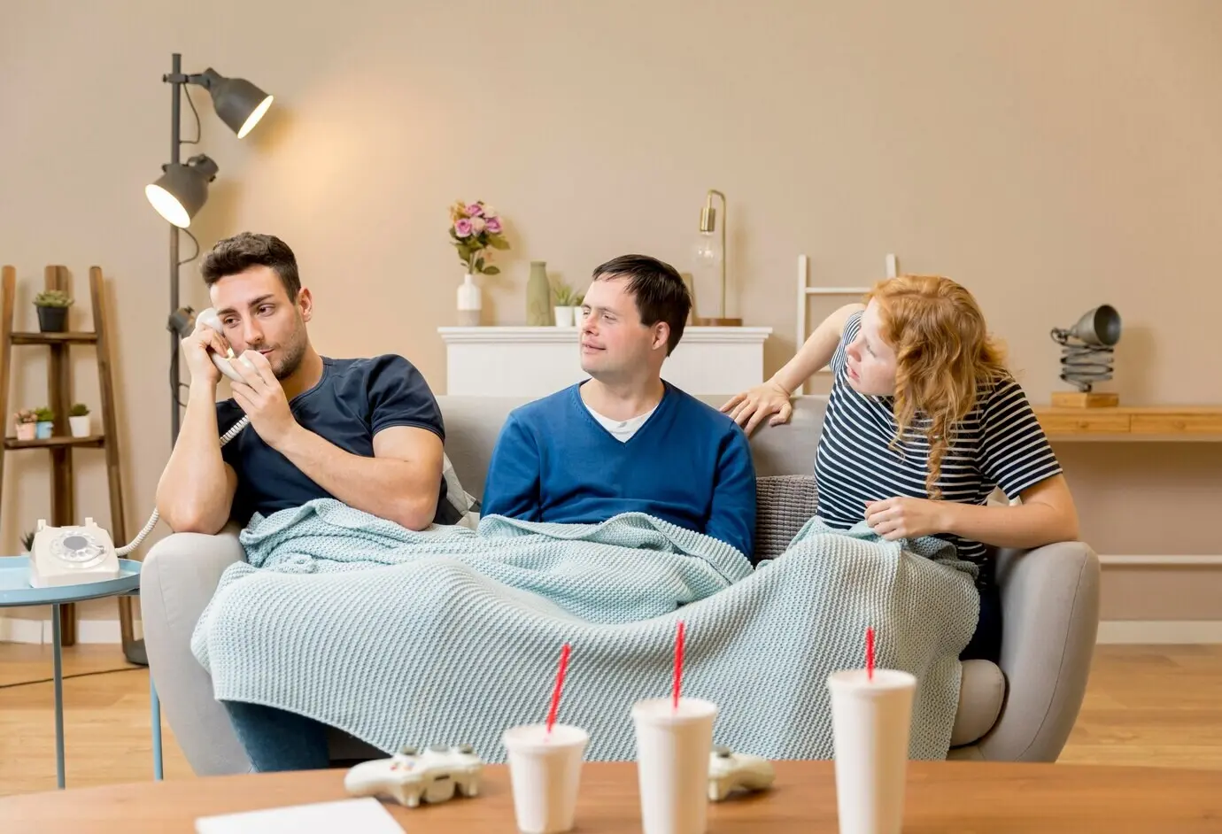 Drei Freunde auf einem Sofa mit einer Decke und Bechern mit Softdrinks.